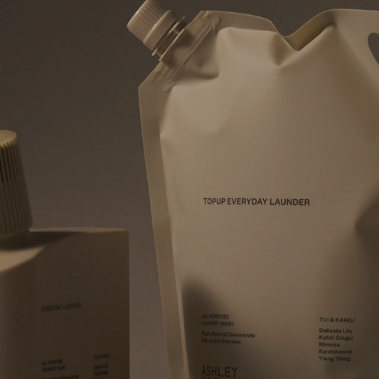 Ashley Topup Everyday Launder refill pouch and bottle in a matching warm off-white color, photographed against a dark gray studio background.