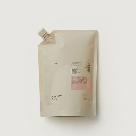 A refill pouch with a white flip-top cap, featuring a minimalist design in warm beige with a small pink label block and black text, including the brand name 'ASHLEY & CO'.