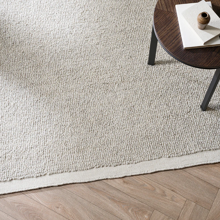 Beige rug on a wooden floor with a small round table in the corner. 100% NZ Wool