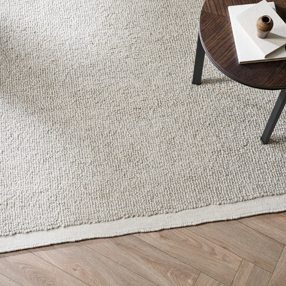 Beige rug on a wooden floor with a small round table in the corner. 100% NZ Wool