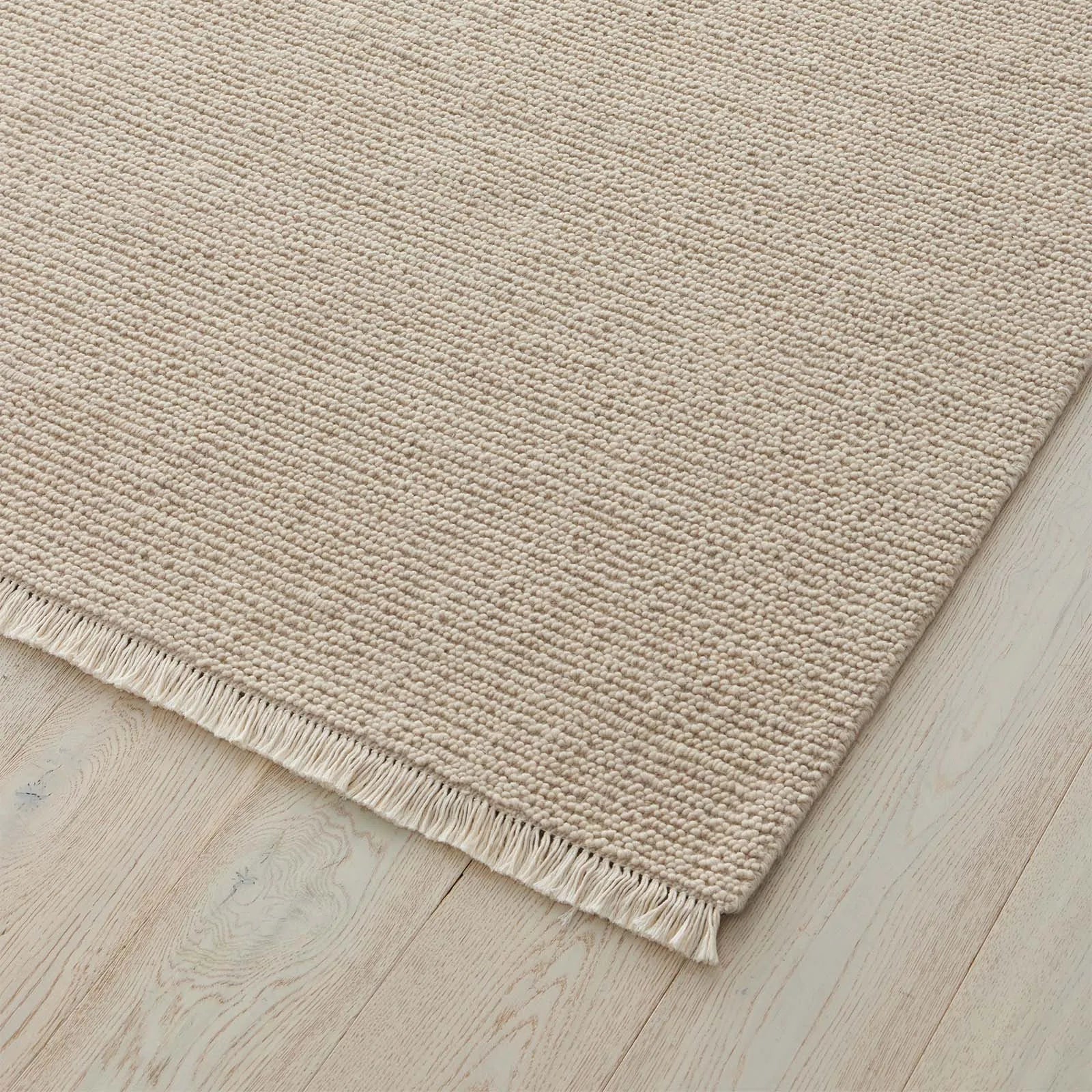 Beige rug with a textured pattern and fringe on a wooden floor. 2x3 3x4. 100% NZ wool