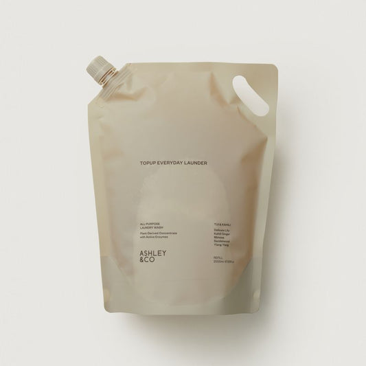 Ashley Topup Everyday Launder refill pouch and bottle in a matching warm off-white color, photographed against a dark gray studio background.