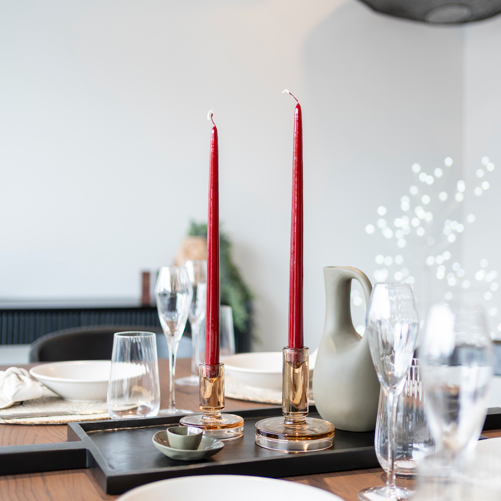 Dining table setting with red candles, plates, and glasses in a modern kitchen.