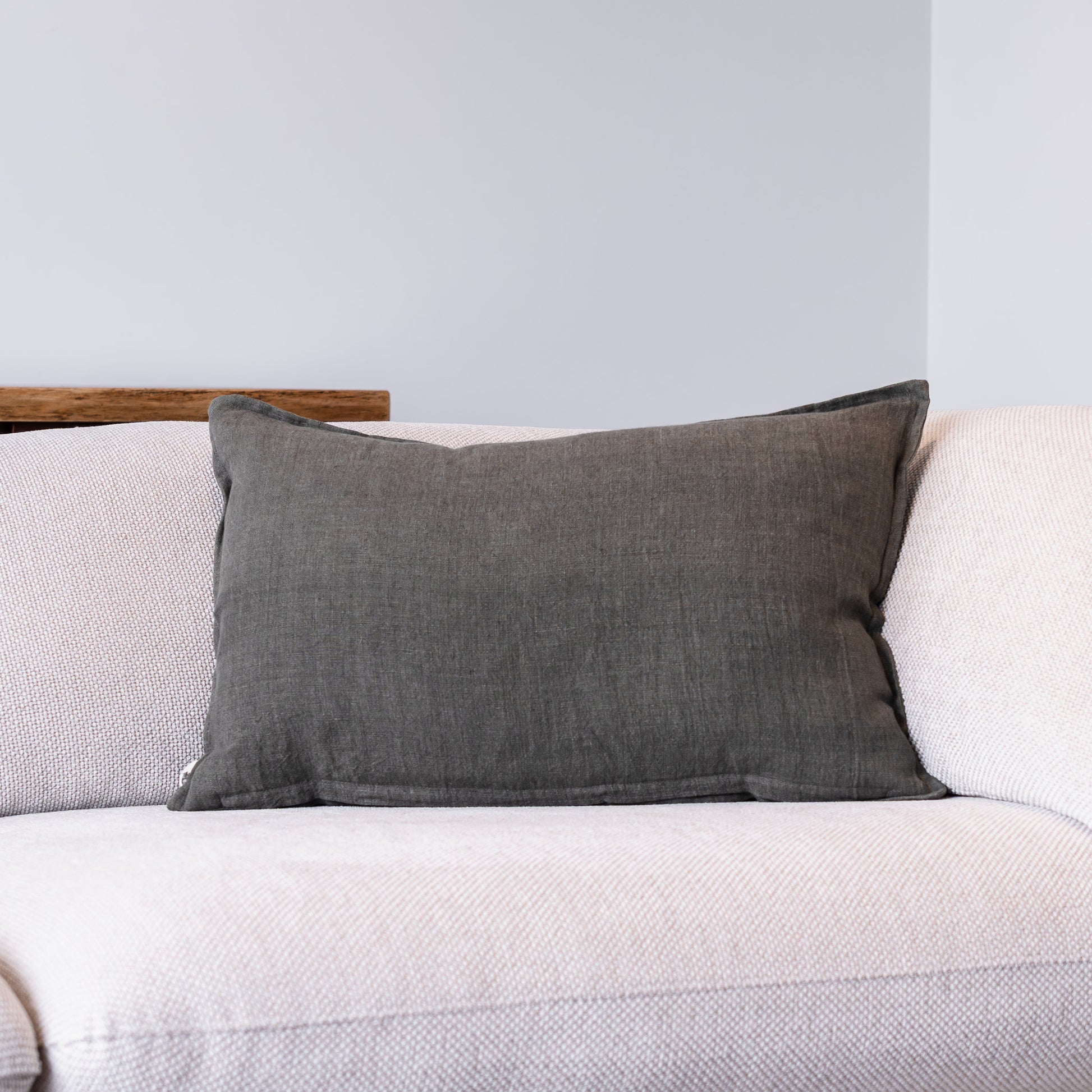 A dark gray textured throw pillow resting on a light beige textured sofa against a neutral gray wall.