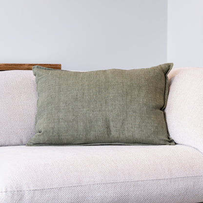An olive green textured throw pillow resting on a light beige textured sofa against a neutral gray wall.