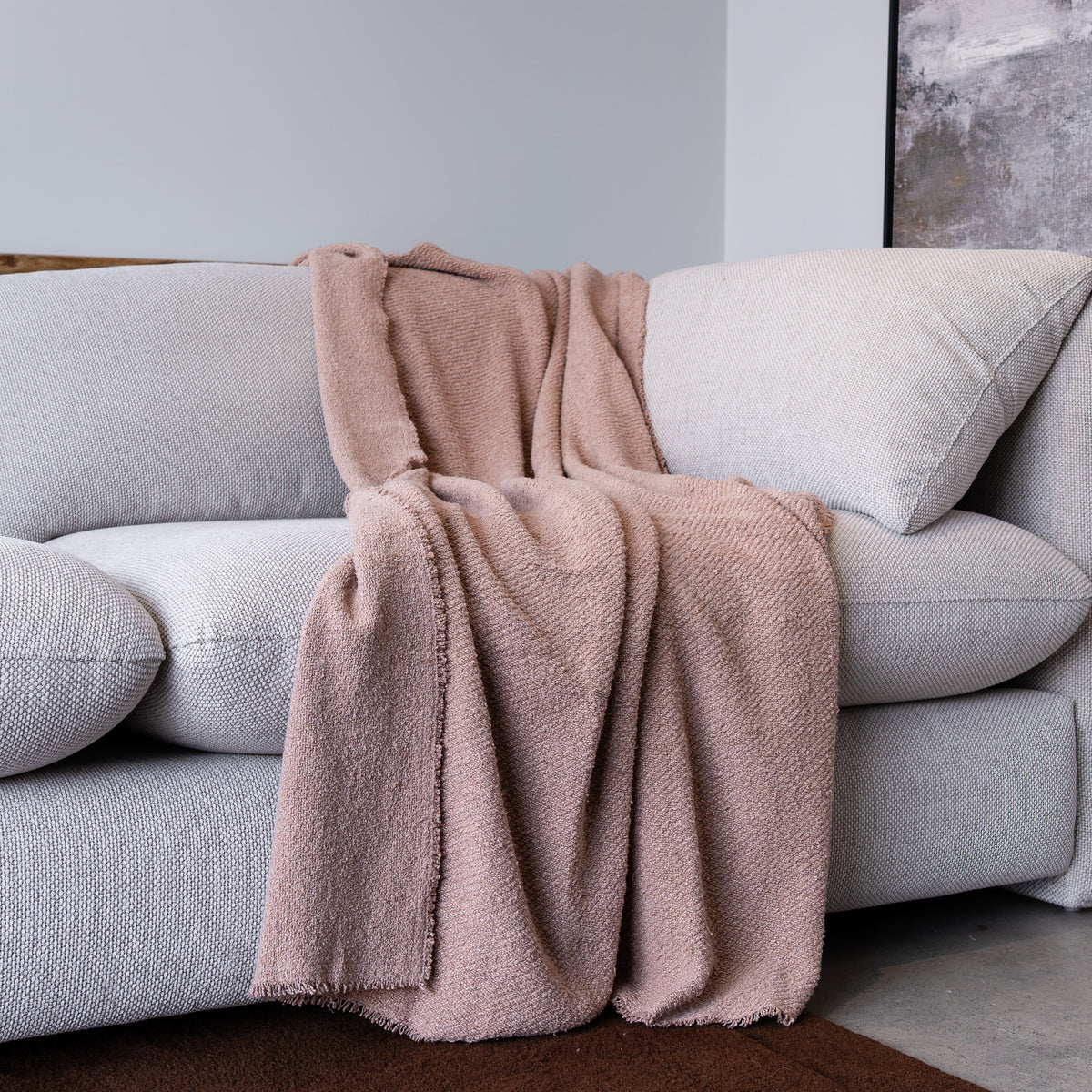 A dusty pink textured throw blanket is draped over a light gray fabric sofa in a modern living room setting.