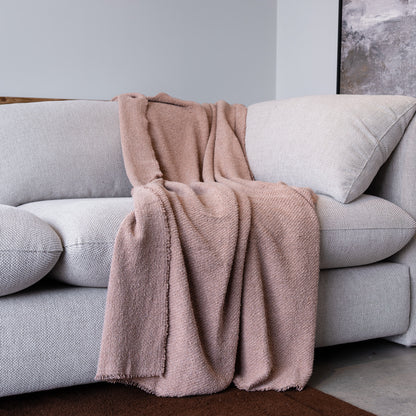 A dusty pink textured throw blanket is draped over a light gray fabric sofa in a modern living room setting.